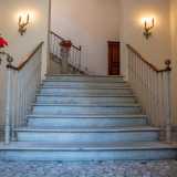 Accediamo all�atrio illuminato da due lampioncini dorati e occupato da un�elegante scala in marmo delimitata da colonnine che sorreggono due vasi